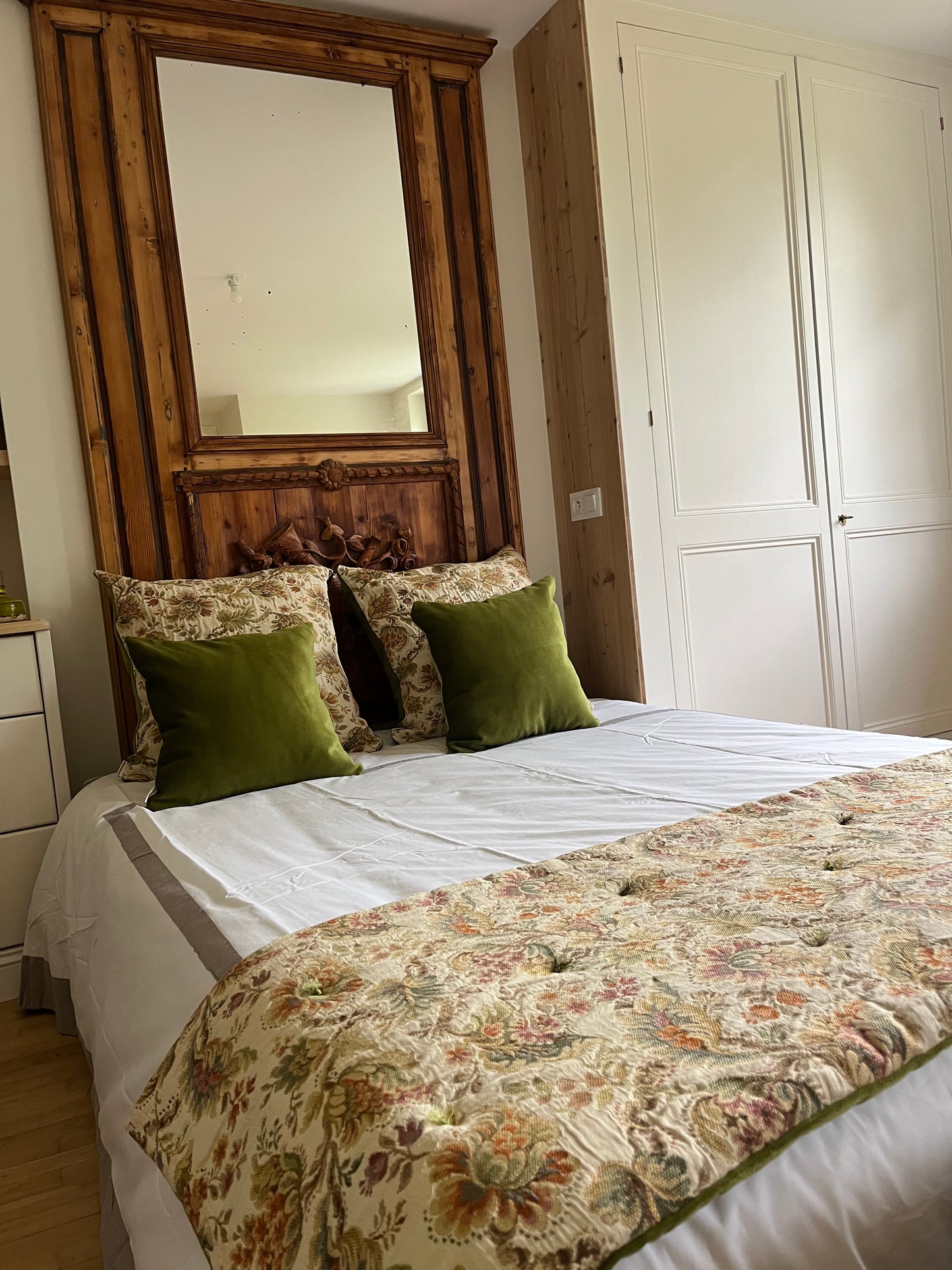 Bedroom with floral bedding, green pillows, and a large wooden mirror.