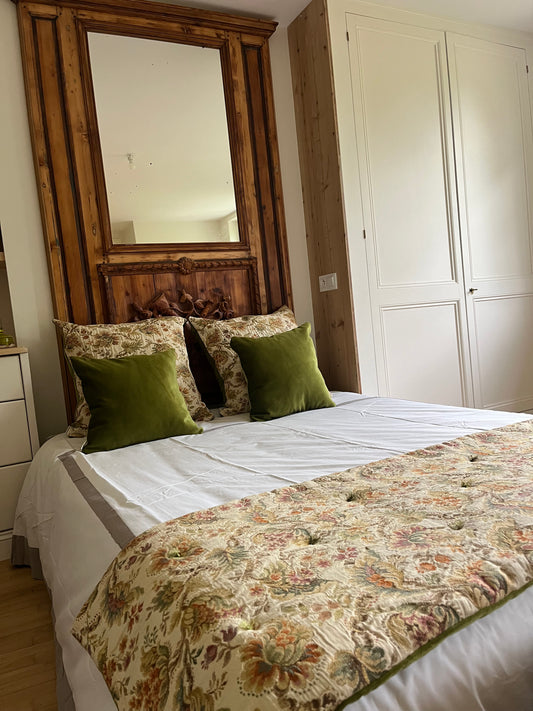 Bedroom with floral bedding, green pillows, and a large wooden mirror.