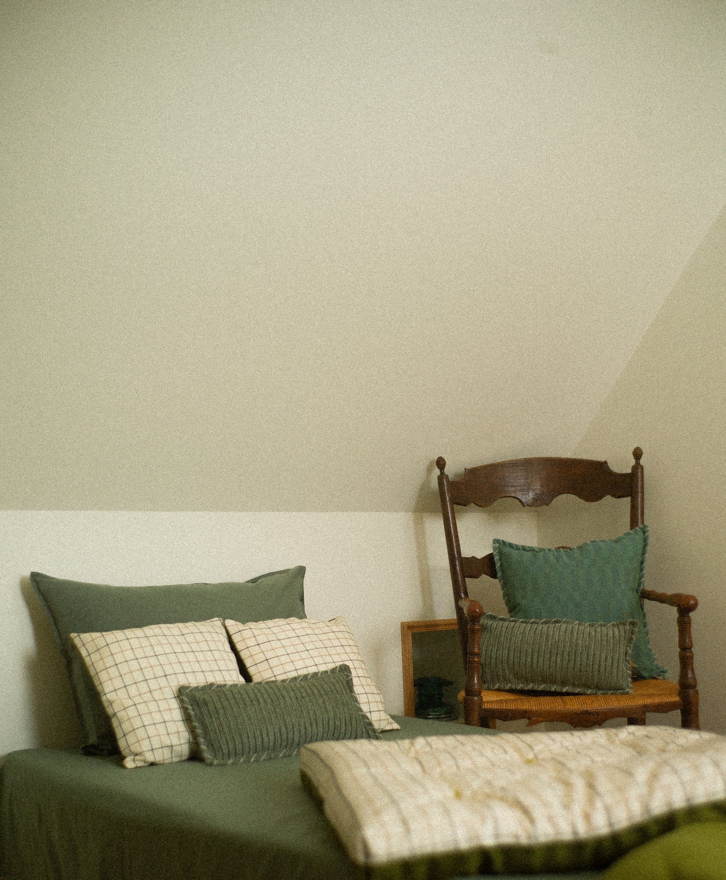 Bed with green and checkered pillows and a wooden chair.