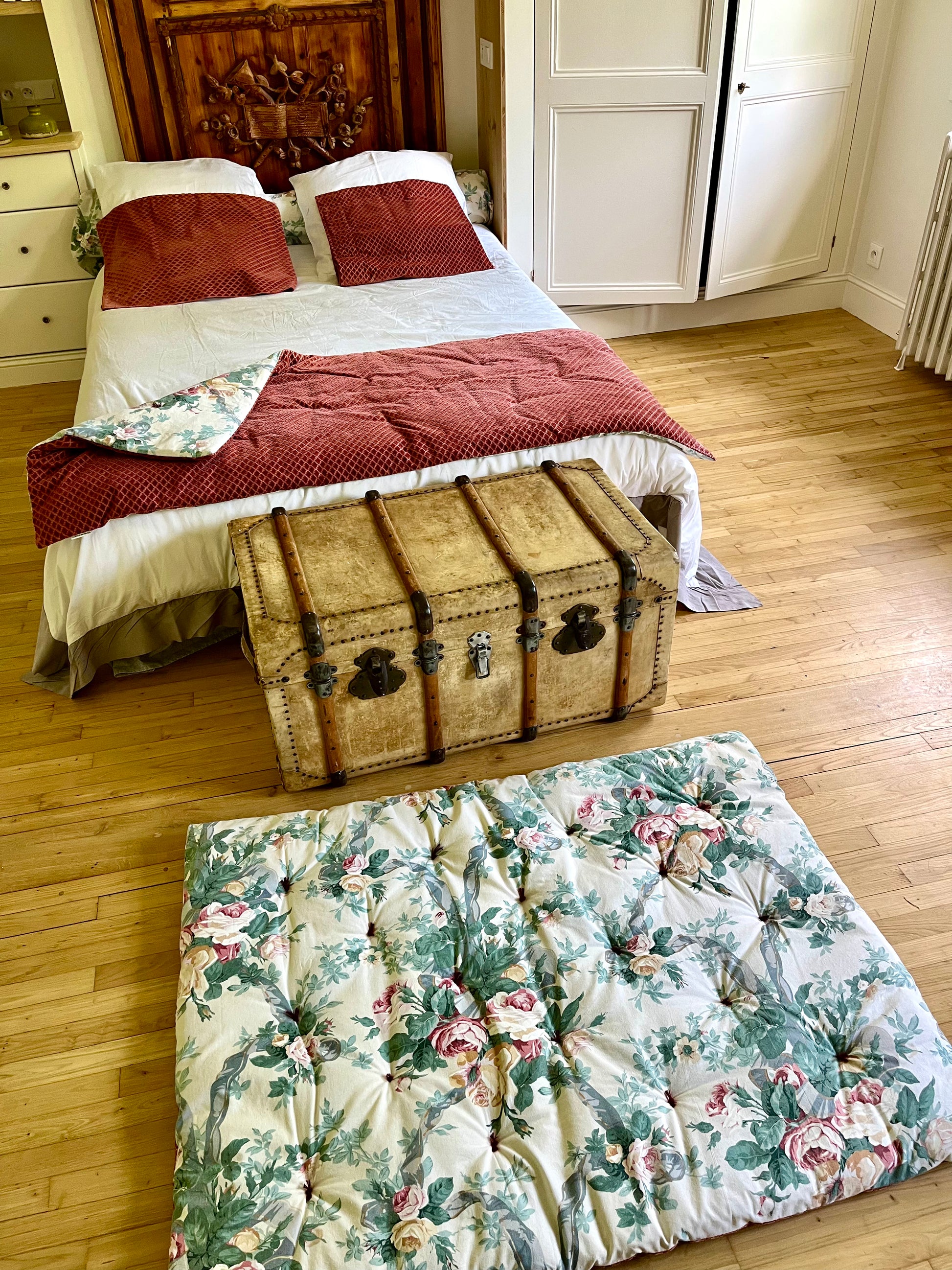 Bedroom with floral mattress cover, wooden trunk, and wardrobe.