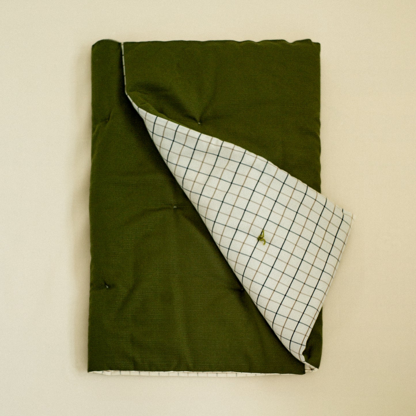 Folded green quilt with a white checkered pattern quilted and filled with sheep wool.