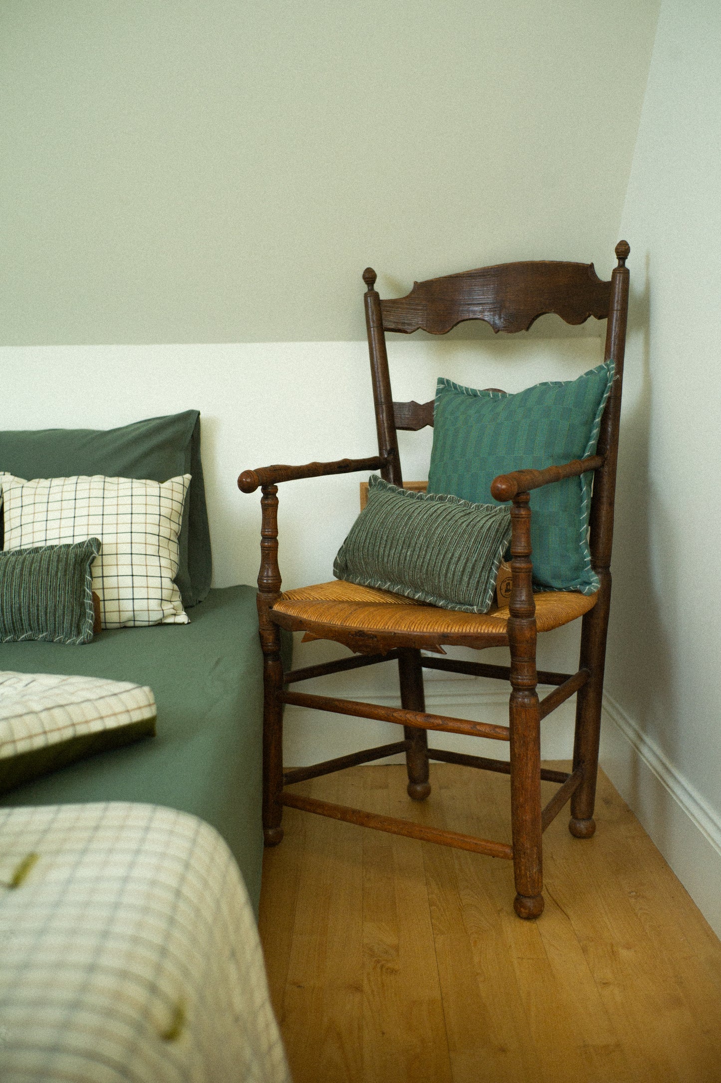 Wooden chair with green cushions against a white wall