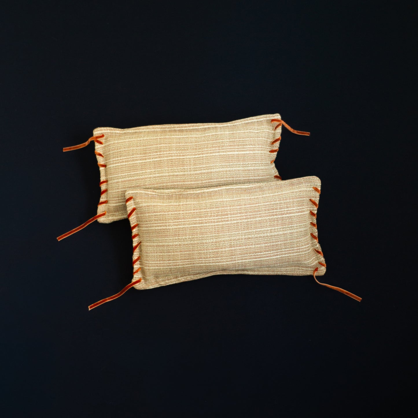 Two woven cushions with orange accents and velvet ribbon detail