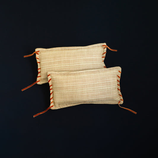 Two woven cushions with orange accents and velvet ribbon detail