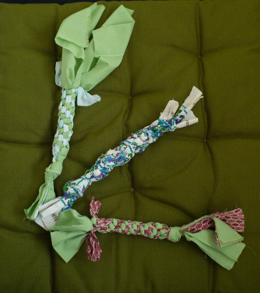Three braided dog toys with colorful patterns on a green cushion.