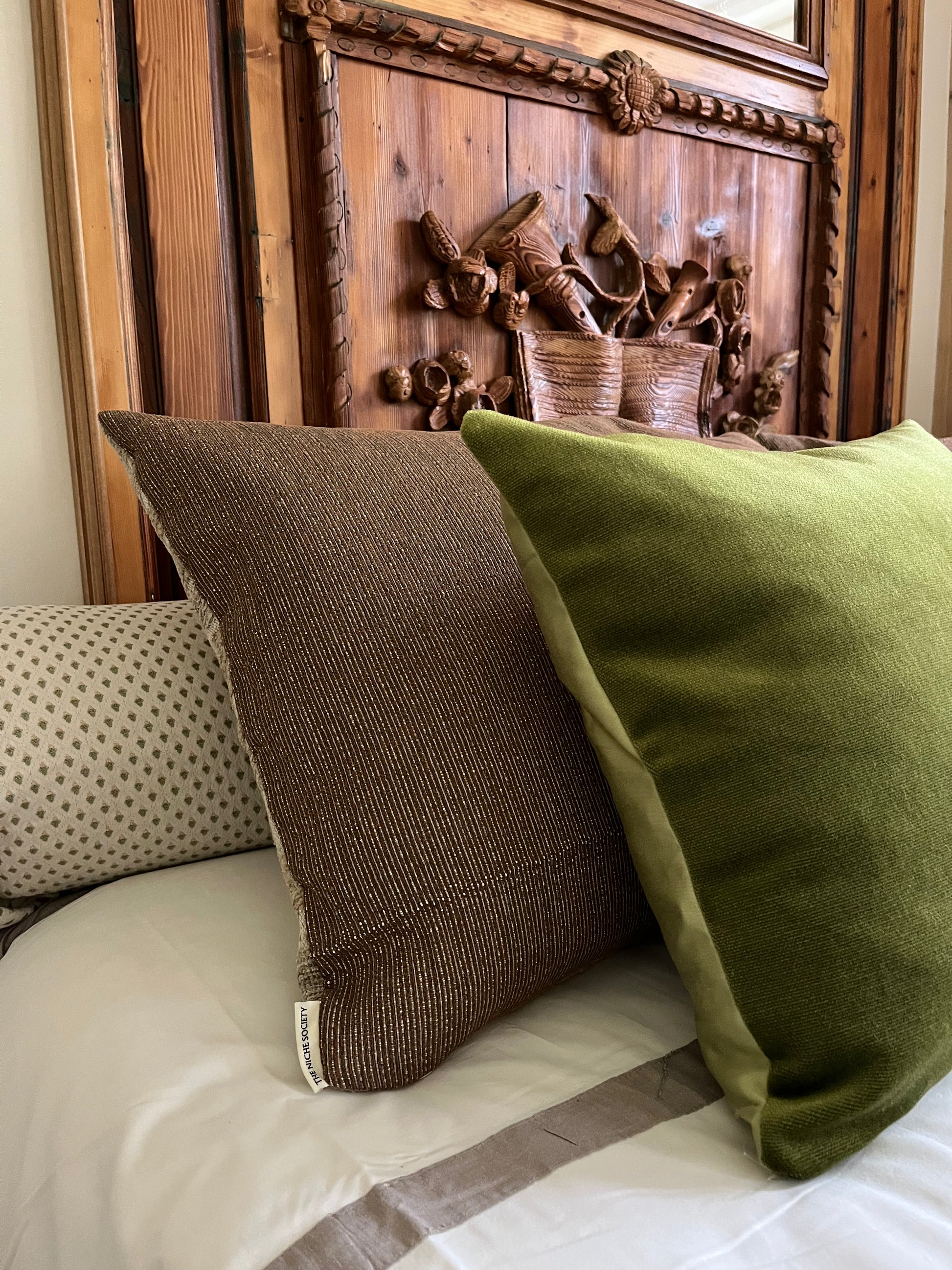 Two pillows, one brown and one green, on a bed with a wooden headboard.