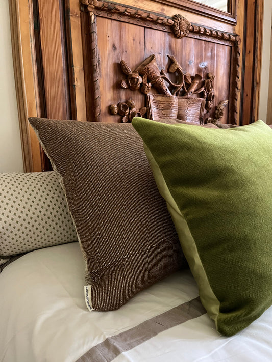Two pillows, one brown and one green, on a bed with a wooden headboard.